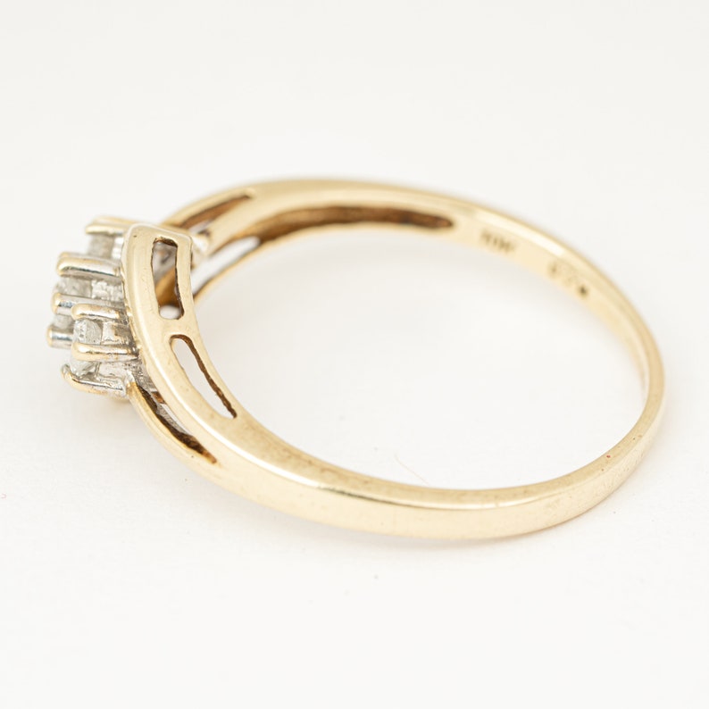 May include: A gold ring with a cluster of small, clear gemstones. The ring has a split shank design and is set against a white background. The ring is marked "14K" and "585".