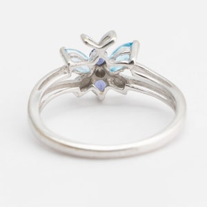 Pu&ograve; includere: Un anello d'argento con un designo a forma di fiore blu e viola. L'anello &egrave; incastonato con diverse piccole pietre preziose.