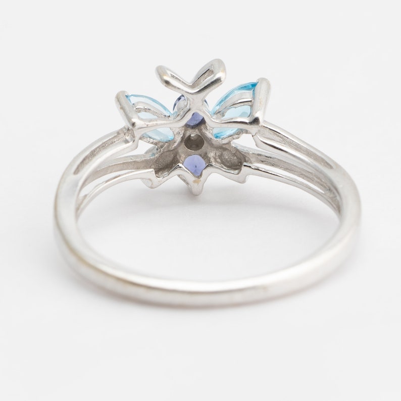 Pu&ograve; includere: Un anello d'argento con un designo a forma di fiore blu e viola. L'anello &egrave; incastonato con diverse piccole pietre preziose.