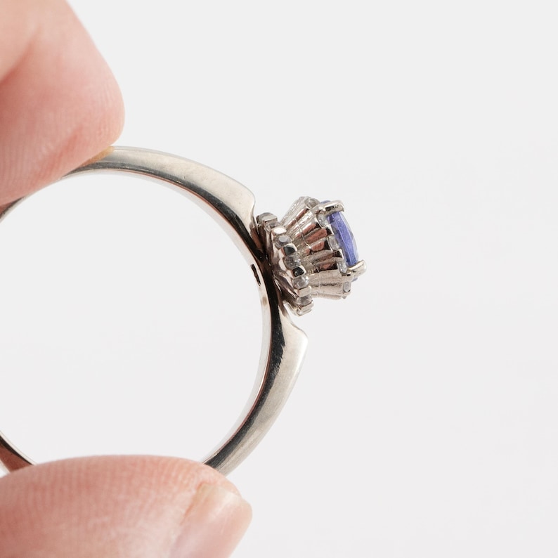 May include: A silver ring with a blue gemstone set in a crown of smaller diamonds.