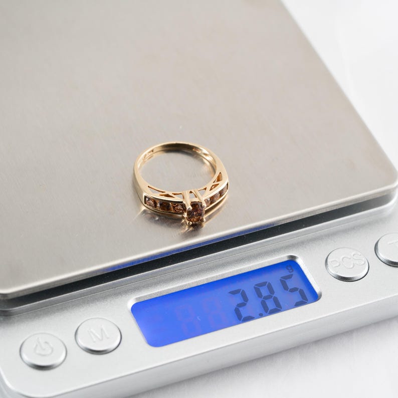 Puede incluir: Un anillo de oro con piedras preciosas marrones en una b&aacute;scula digital que marca 2,85 gramos.