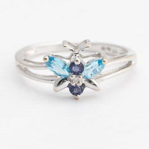 Pu&ograve; includere: Un anello d'argento con un design a farfalla con pietre preziose blu e viola. La farfalla ha due pietre di forma marquise blu chiaro e tre pietre viola pi&ugrave; piccole.
