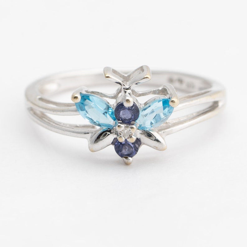 Pu&ograve; includere: Un anello d'argento con un design a farfalla con pietre preziose blu e viola. La farfalla ha due pietre di forma marquise blu chiaro e tre pietre viola pi&ugrave; piccole.