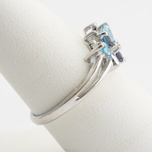 Pu&ograve; includere: Un anello d'argento con un gruppo di pietre preziose blu e trasparenti. L'anello &egrave; posto su un espositore bianco.