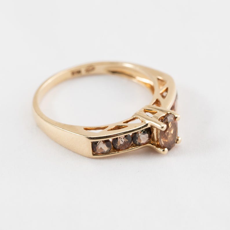 Puede incluir: Un anillo de oro con una piedra preciosa marr&oacute;n en el centro y piedras preciosas marrones m&aacute;s peque&ntilde;as engastadas en una banda alrededor de la piedra central.