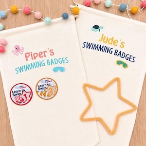 May include: Two off-white canvas wall banners featuring embroidered text and graphics. One banner reads Piper's SWIMMING BADGES with a pink octopus and blue goggles. The other reads Jude's SWIMMING BADGES with a turtle and yellow goggles.