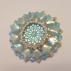 May include: A light blue and silver beaded flower brooch with a geometric design in the center.