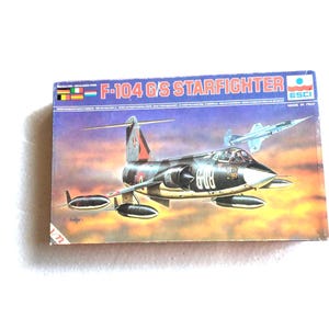 以下が含まれることがあります： F-104 GS スターファイター航空機の模型キットボックス。ボックスには、飛行中のジェット機の詳細なイラストが描かれており、「F-104 GS STARFIGHTER」の文字が大きく表示されています。 ヴィンテージアイテムです。
