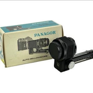 May include: Vintage Panagor Auto-Bellowscope camera accessory with original box. The box is beige with a teal top and features a graphic of the camera accessory. The accessory is black and silver.