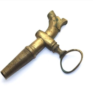 May include: An antique brass tap with a textured, threaded spout and a curved handle. The tap has a vintage appearance with signs of age and wear, suggesting it is an older piece. The brass has a warm, golden hue.