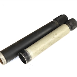 May include: Two cylindrical objects, one black and one off-white, are positioned diagonally against a white background. Both have a metallic rim at one end and a textured, black cap at the other. The black cylinder is longer than the off-white one.