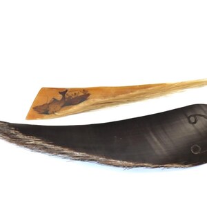 May include: Two handcrafted items are displayed against a white background. One is a dark, curved object with a textured edge. The other is a light-colored, rectangular piece with a boat illustration. Both appear to be made of natural materials.