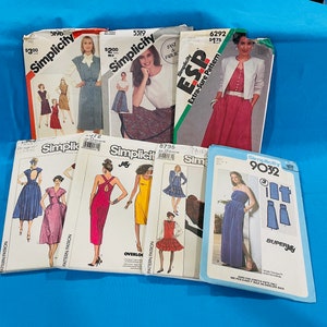 May include: A collection of Simplicity sewing patterns for various clothing styles. The patterns include dresses, skirts, and tops. The patterns are in various colours, including red, blue, and green. The patterns are labelled with the Simplicity logo and the pattern number.