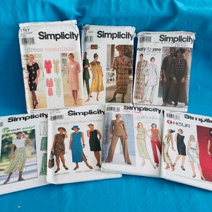 May include: A selection of Simplicity sewing pattern envelopes. The patterns showcase diverse dress and outfit designs, including dresses, skirts, and trousers. The envelopes are white with images of the finished garments and text such as "dress essentials" and "easy to sew".