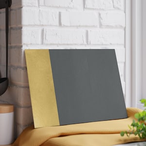 May include: A rectangular chopping board with a gold vertical stripe on the left and a dark grey surface on the right. The board is on a yellow cloth.