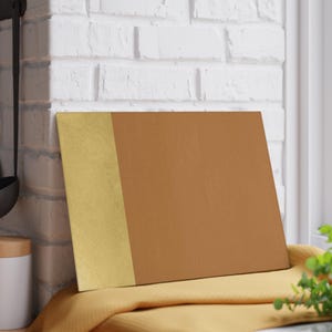 May include: A rectangular cutting board with a gold vertical stripe on the left and a brown surface on the right. The board rests on a yellow cloth. The cutting board is likely for kitchen use.