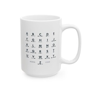 Könnte beinhalten: Weißer Keramikbecher mit dem Morsecode-Alphabet in Schwarz. Die Buchstaben A bis Z werden mit ihren entsprechenden Punkten und Strichen dargestellt. Die Worte "MORSE CODE" sind am Boden des Bechers aufgedruckt.
