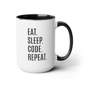 Peut inclure: Mug en céramique blanche avec intérieur, anse et bord noirs. Le mug affiche le texte "EAT. SLEEP. CODE. REPEAT." en gras noir. Conçu pour les boissons chaudes ou froides.