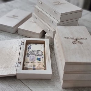 Op de afbeelding: Verschillende lichtgekleurde houten kisten, waarvan sommige open zijn om stapels Oekraïense 500 hryvnia-bankbiljetten te laten zien. De kisten hebben een scharnierend deksel en een eenvoudig ontwerp. De tekst "GARDEN HOTEL" is zichtbaar.
