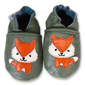 Puede incluir: Un par de zapatos de beb&eacute; de cuero verde con un dise&ntilde;o de zorro. El zorro es naranja con la cara blanca y la punta de la cola blanca.