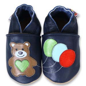 Puede incluir: Un par de zapatos de beb&eacute; de cuero azul con un dise&ntilde;o de osito de peluche en un zapato y un dise&ntilde;o de globo en el otro.
