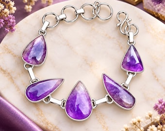 May include: A silver-toned metal bracelet featuring four polished, teardrop-shaped purple amethyst gemstones set in smooth bezels. The bracelet includes a series of circular silver links and a hook-style clasp closure, creating a continuous chain design.