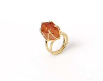 May include: A gold ring with a large, orange, irregularly shaped gemstone set in a delicate wire cage.