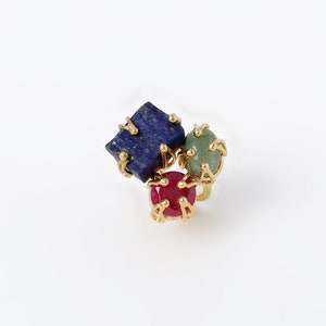 Puede incluir: Un anillo de oro con tres piedras preciosas: un lapislázuli azul, una piedra verde y un rubí rojo.
