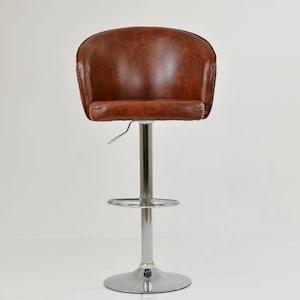 May include: A brown leather bar stool with a curved back and a chrome base. The stool features a footrest and a height-adjustable mechanism. The seat is a rich brown, and the base is a shiny silver. The height is adjustable.