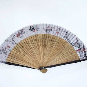 May include: A folding hand fan with a bamboo frame and a white paper panel. The panel features a floral design with red and gray accents, and a black Japanese character. The fan is open, displaying its full shape.