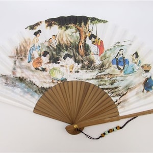 May include: A hand fan with a painted scene of people in traditional clothing, enjoying leisure activities. The fan has a wooden handle and a decorative tassel. The artwork features a tree and figures in various poses, with a color palette of blues, greens, and browns.