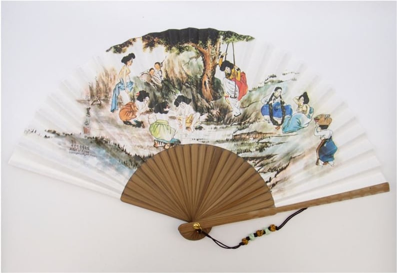 May include: A hand fan with a painted scene of people in traditional clothing, enjoying leisure activities. The fan has a wooden handle and a decorative tassel. The artwork features a tree and figures in various poses, with a color palette of blues, greens, and browns.