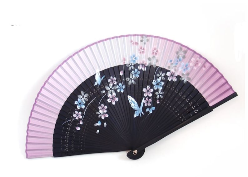 May include: A decorative folding fan with a black wooden frame and a light purple and white fabric. The fan features a floral design with butterflies in shades of blue and pink. The fan is open, displaying its full design.
