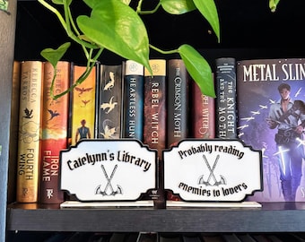 Spersonalizowana tabliczka dekoracyjna na półkę na książki – znak o tematyce fantasy, prawdopodobnie czytający wrogów kochankom lub z niestandardowym tekstem