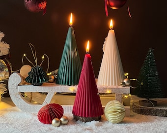 May include: Three Christmas tree-shaped candles, one green, one red, and one white, are arranged on a wooden sled with a white finish. The candles are lit and the sled is decorated with small red and gold ornaments.