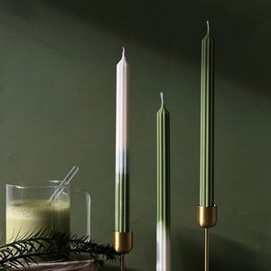 Pode incluir: Tr&ecirc;s velas c&oacute;nicas verdes e brancas em casti&ccedil;ais dourados sobre uma superf&iacute;cie de madeira. As velas t&ecirc;m um design degradado verde e branco.