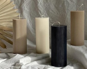 May include: Four pillar candles with a ribbed design. The candles are in beige, white, and black.