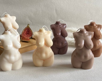 May include: Five different colored candles shaped like the human torso. The candles are arranged in a row on a white surface.