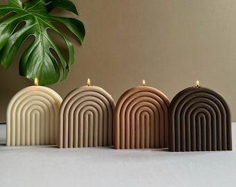 May include: Four arch-shaped candles in different shades of brown, beige, and white. The candles are arranged in a row from left to right, with the white candle on the left and the darkest brown candle on the right.
