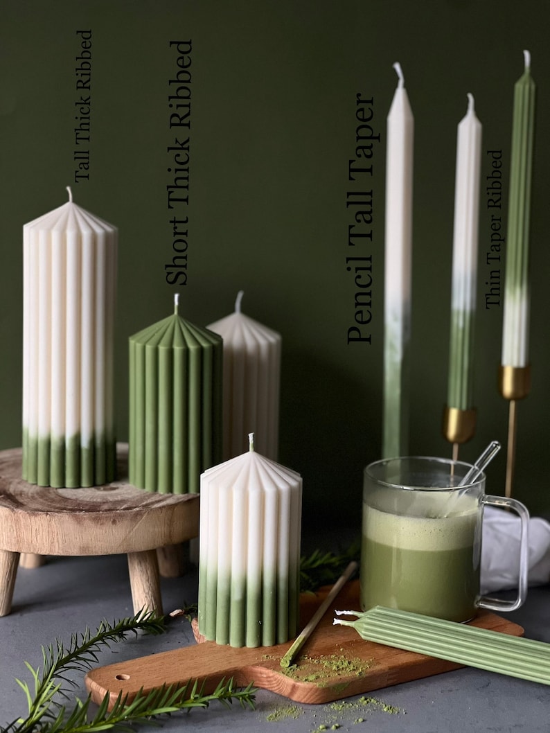 Pode incluir: Conjunto de velas caneladas verdes e brancas em v&aacute;rios tamanhos e estilos, incluindo velas caneladas grossas altas, velas caneladas grossas curtas, velas finas altas e velas caneladas finas. As velas s&atilde;o exibidas em uma superf&iacute;cie de madeira com uma x&iacute;cara de ch&aacute; verde.
