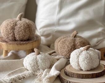 May include: Three fuzzy pumpkins, two brown and one white, are arranged on a wooden surface. The pumpkins are made of a soft, plush material and have a realistic shape. They are a decorative accent for a home or a fall-themed event.