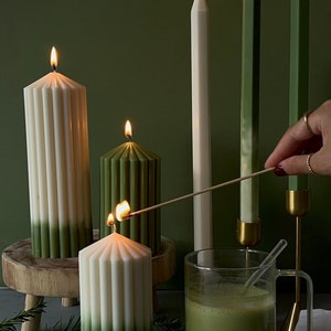 Pode incluir: Quatro velas, duas verdes e duas brancas, com um efeito degrad&ecirc; verde, est&atilde;o acesas e dispostas sobre uma superf&iacute;cie de madeira. Uma caneca de vidro cheia de uma bebida verde fica na frente das velas. P&oacute; verde &eacute; espalhado sobre a superf&iacute;cie.