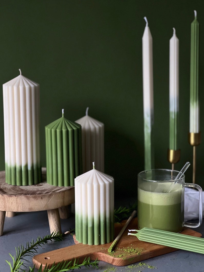 Pode incluir: Um conjunto de velas verde e branco degrad&ecirc; com um design canelado. As velas est&atilde;o dispostas sobre uma superf&iacute;cie de madeira com uma x&iacute;cara de ch&aacute; verde e uma t&aacute;bua de cortar de madeira.