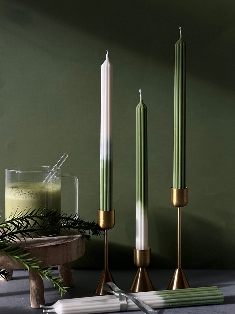 Pode incluir: Tr&ecirc;s velas c&oacute;nicas verdes e brancas em casti&ccedil;ais dourados sobre uma superf&iacute;cie de madeira. As velas t&ecirc;m um design degradado verde e branco.