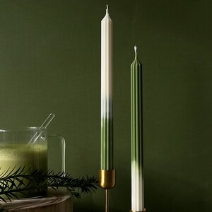Pode incluir: Duas velas c&oacute;nicas verde e branco ombre em casti&ccedil;ais dourados sobre um suporte de madeira. As velas est&atilde;o sobre um fundo verde.