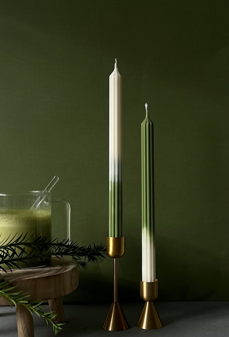 Pode incluir: Duas velas c&oacute;nicas verde e branco ombre em casti&ccedil;ais dourados sobre um suporte de madeira. As velas est&atilde;o sobre um fundo verde.