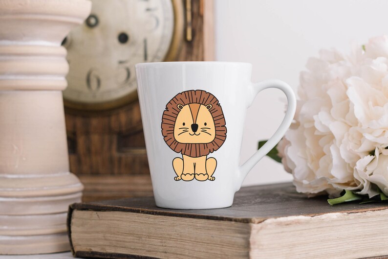 May include: White ceramic mug with a cartoon illustration of a brown lion with a yellow face. The lion is sitting down with its paws in front of it.