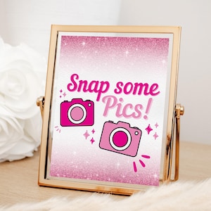 Puede incluir: Un letrero con marco dorado con fondo de purpurina rosa y el texto "Snap some Pics!" en rosa. Dos cámaras de dibujos animados rosas están a cada lado del texto.