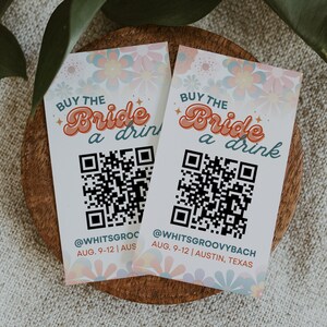 Puede incluir: Dos tarjetas blancas con un diseño floral y el texto "Buy the Bride a drink" en una fuente retro. Cada tarjeta tiene un código QR y el texto "@WHITSGROC AUG. 9-12 | AUS" y "@WHITSGROOVYBACH AUG. 9-12 | AUSTIN, TEXAS".