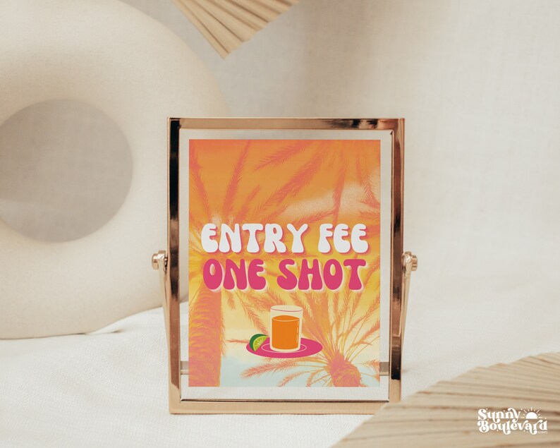 Puede incluir: Un cartel con marco dorado con un fondo tropical y el texto "ENTRY FEE ONE SHOT" en letras rosas. Un vaso de zumo de naranja con una rodaja de lima se encuentra en un plato delante del texto.